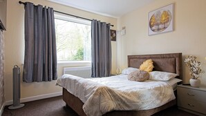 A bedroom with a large bed, a bedside table, a heater, and a window with curtains. - Stylish Five Star Rated Apartment (Manchester)