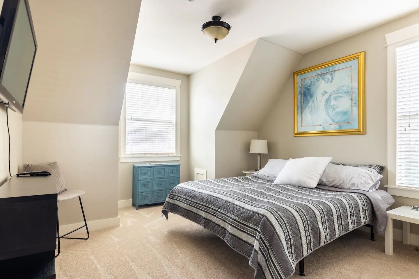 A bedroom with a bed, a dresser, a desk, a lamp, and a painting on the wall.