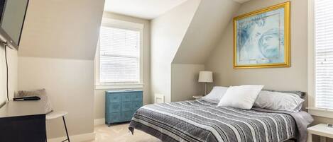 A bedroom with a bed, a dresser, a desk, a lamp, and a painting on the wall.