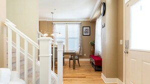 A hallway with a staircase, a dining area with a table and chairs, and a bench.