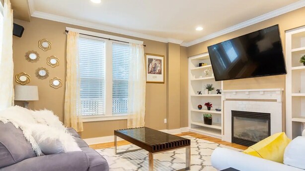 A living room with a sofa, a coffee table, a flat-screen TV, a fireplace, and decorative wall sconces.