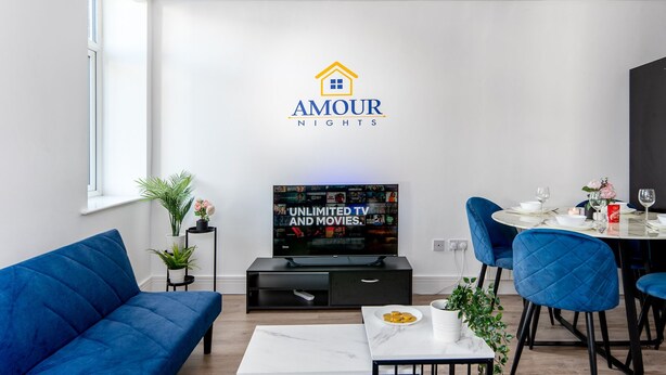En moderne stue med et fladskærms-tv, en sofa, et spisebord med stole, og et logo på væggen.