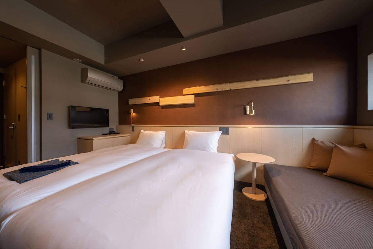 Habitación de hotel con una cama grande, dos mesitas de noche, un televisor y un aire acondicionado instalado en la pared.