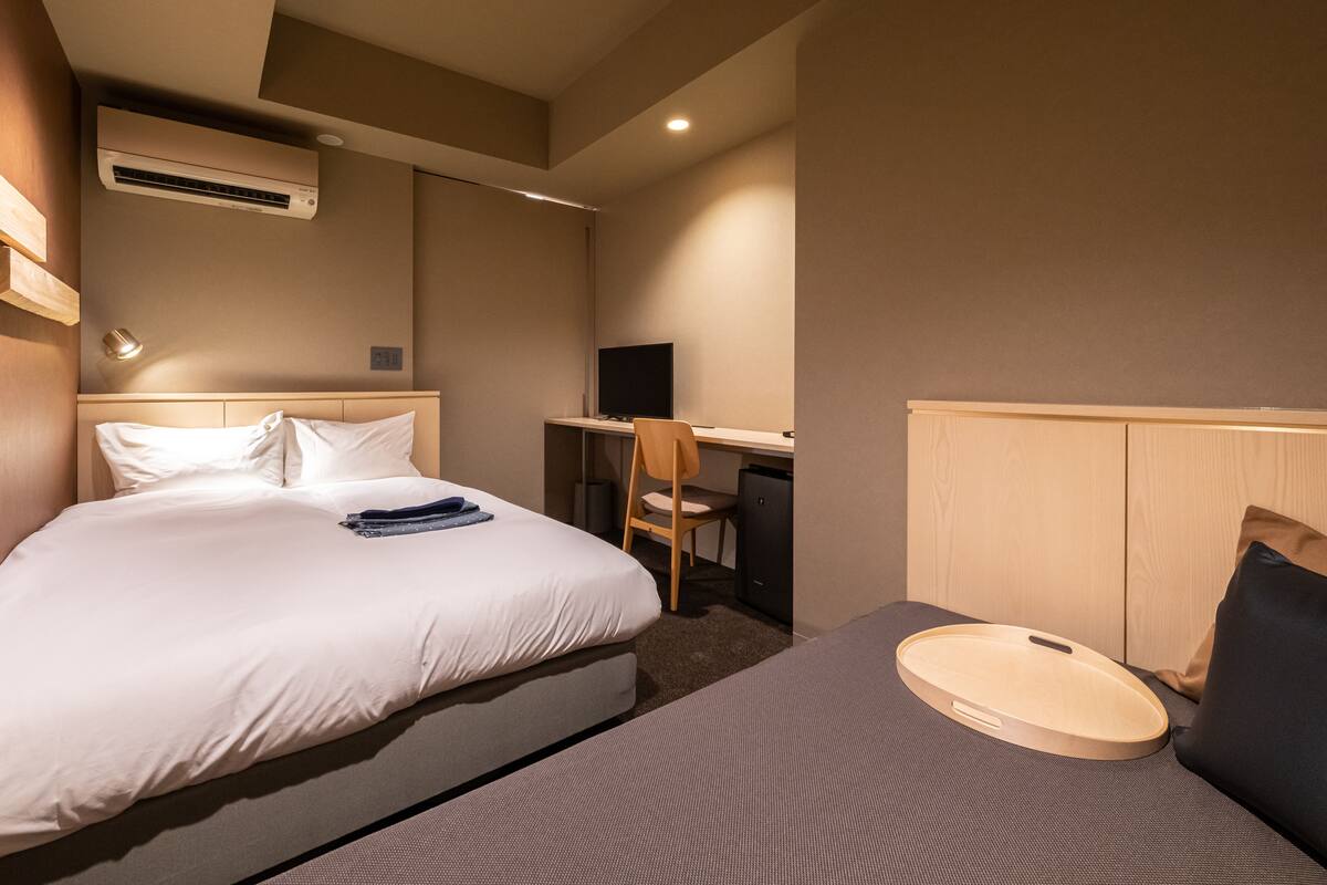 Habitación de hotel con cama, escritorio, silla y equipo de aire acondicionado.