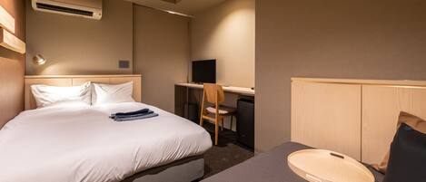 A hotel room with a bed, a desk, a chair, and an air conditioning unit.