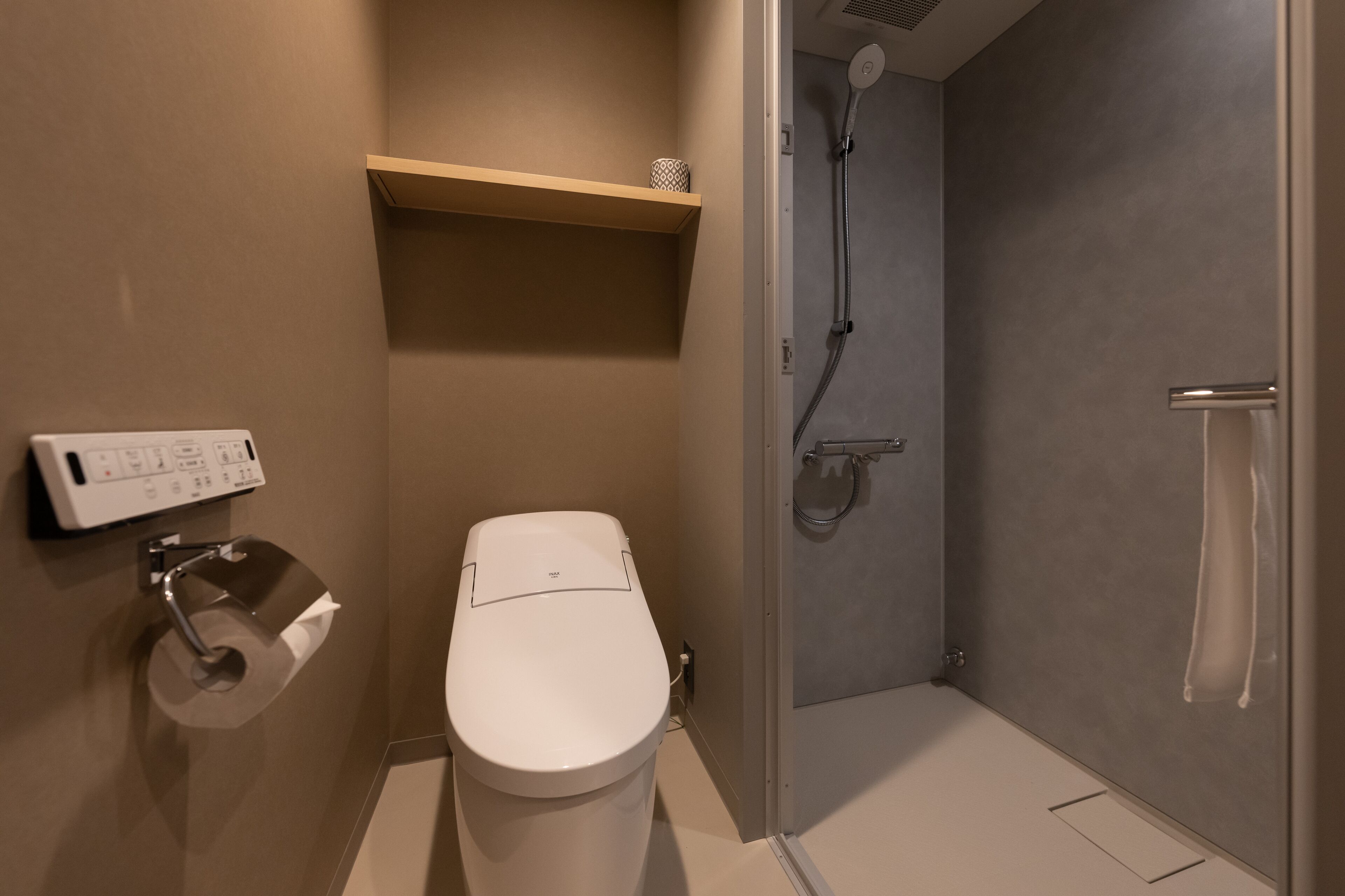 Une salle de bain moderne équipée de toilettes, d’une douche et d’une étagère au-dessus des toilettes.