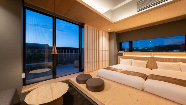 A modern hotel room with a large sliding glass door leading to a balcony, a sofa bed with pillows, a small round table, and a wall-mounted TV. - OnnNakatsugawa (Nakatsugawa)