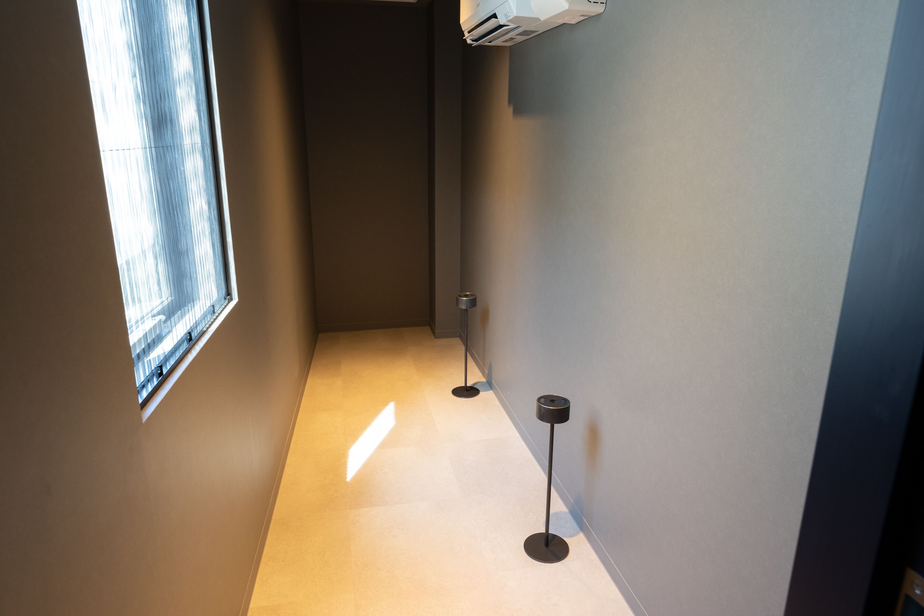Ein schmaler Flur mit einem Fenster links, einer Stehlampe und einer Wand-Klimaanlage.