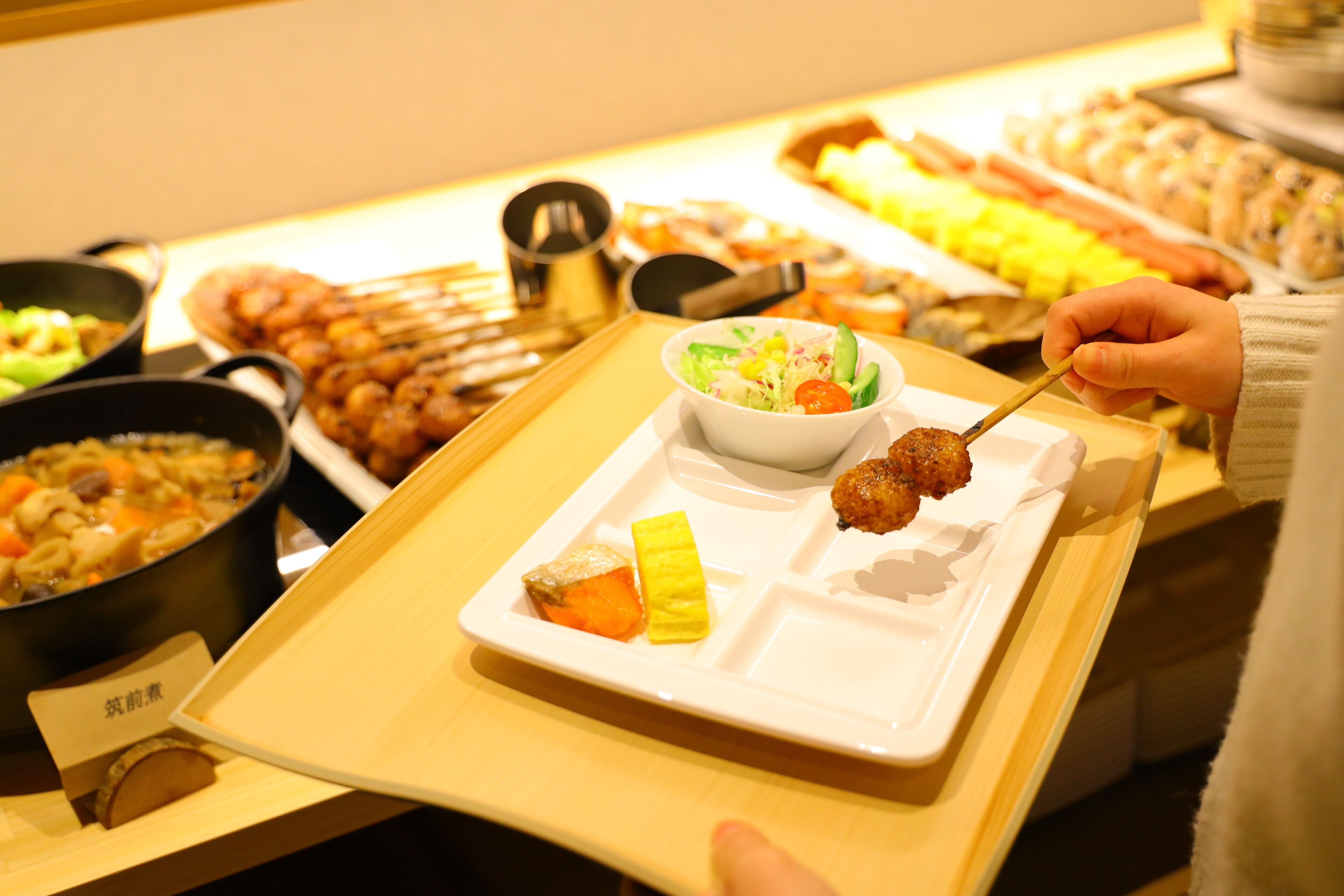 A buffet with various dishes including a bowl of salad, a plate with meatballs and vegetables, and several other food options.