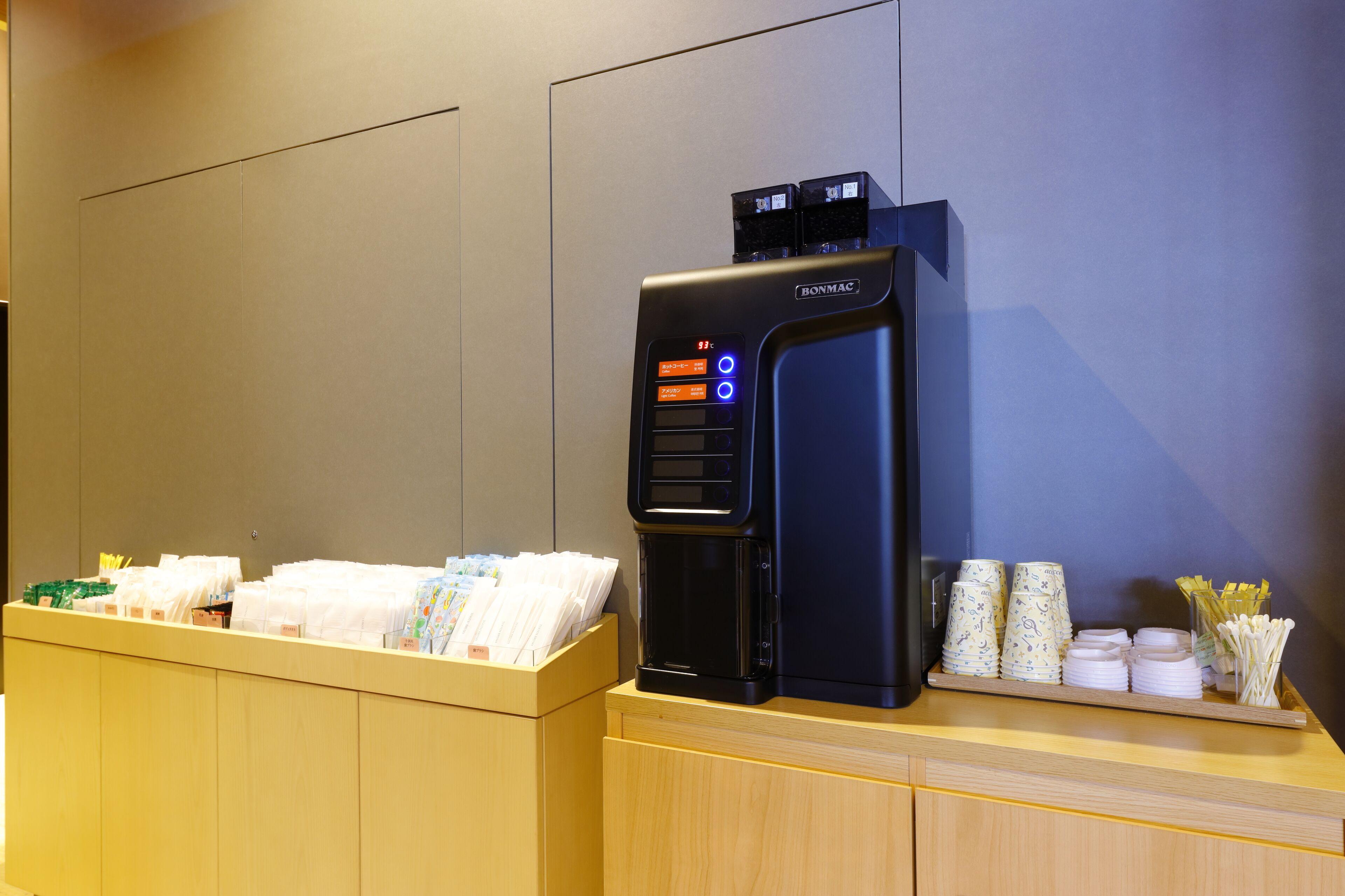 A self-service beverage dispenser with a digital display, a card reader, and a tray with disposable cups and utensils.
