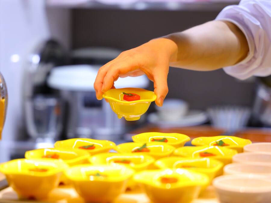 A hand holding a yellow container with a red item inside, placed on a table with multiple yellow containers.