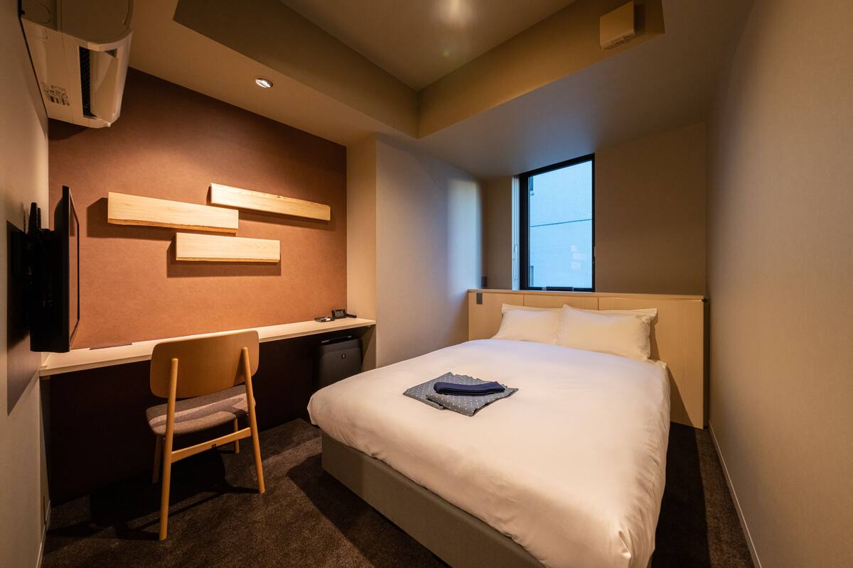 Habitación de hotel con cama, escritorio, silla, ventana y aire acondicionado de pared.