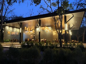 Un edificio moderno con un patio abierto, que cuenta con varias mesas y sillas para comer, rodeado de abundante vegetación.