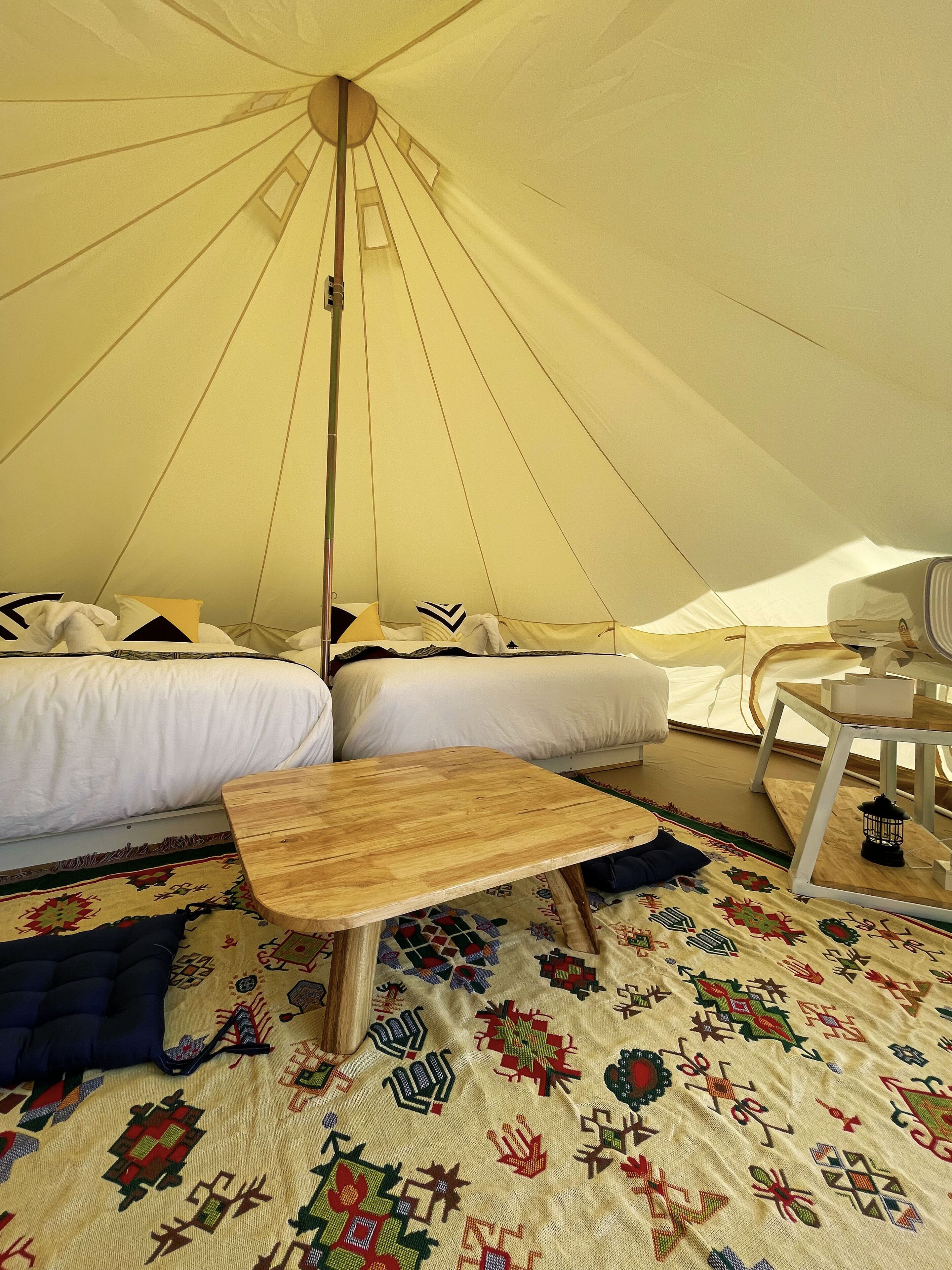 A tent with two beds, a wooden table, and a patterned rug.