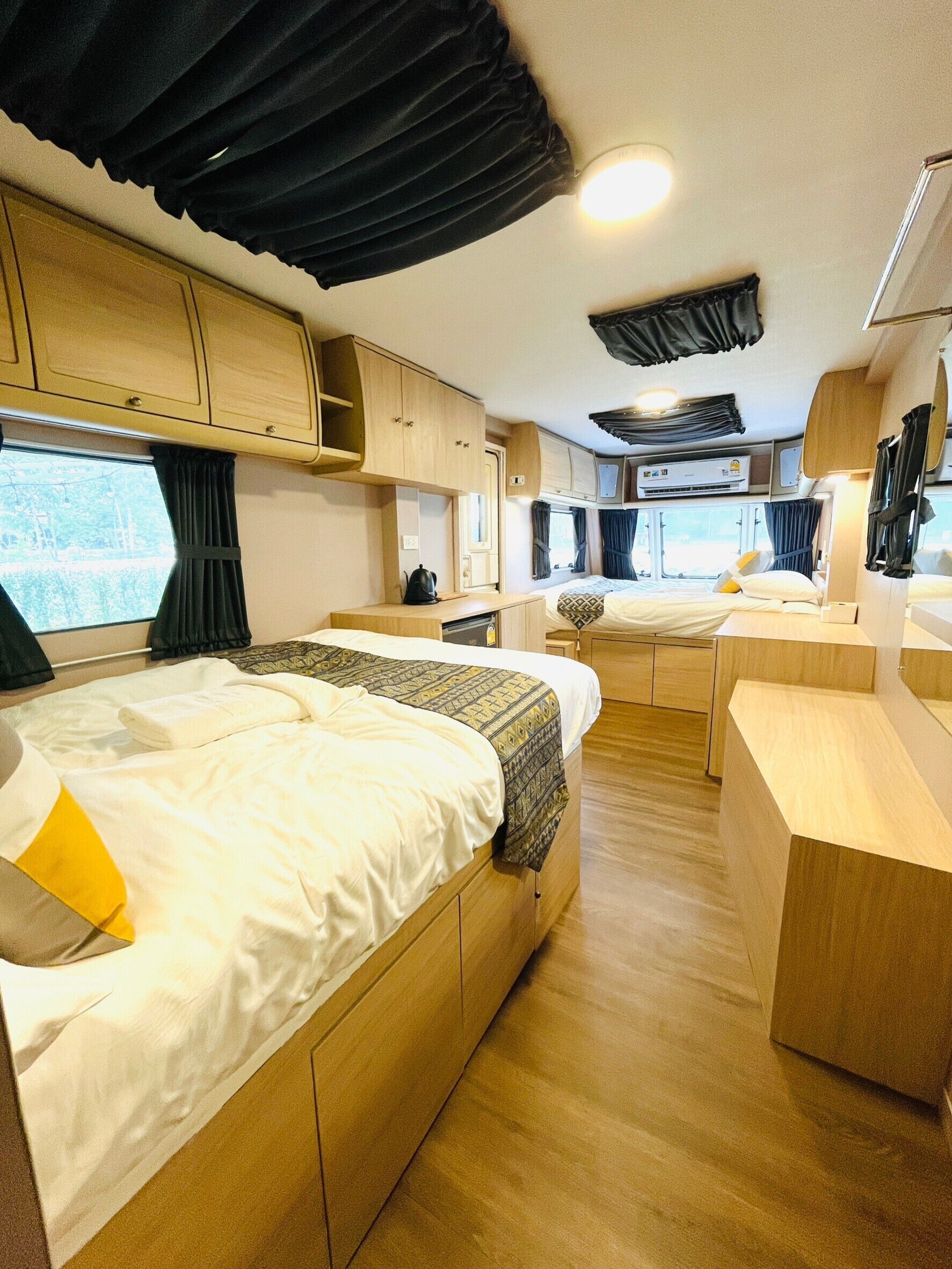 A well-lit RV interior with two beds, a kitchenette, and a bathroom.