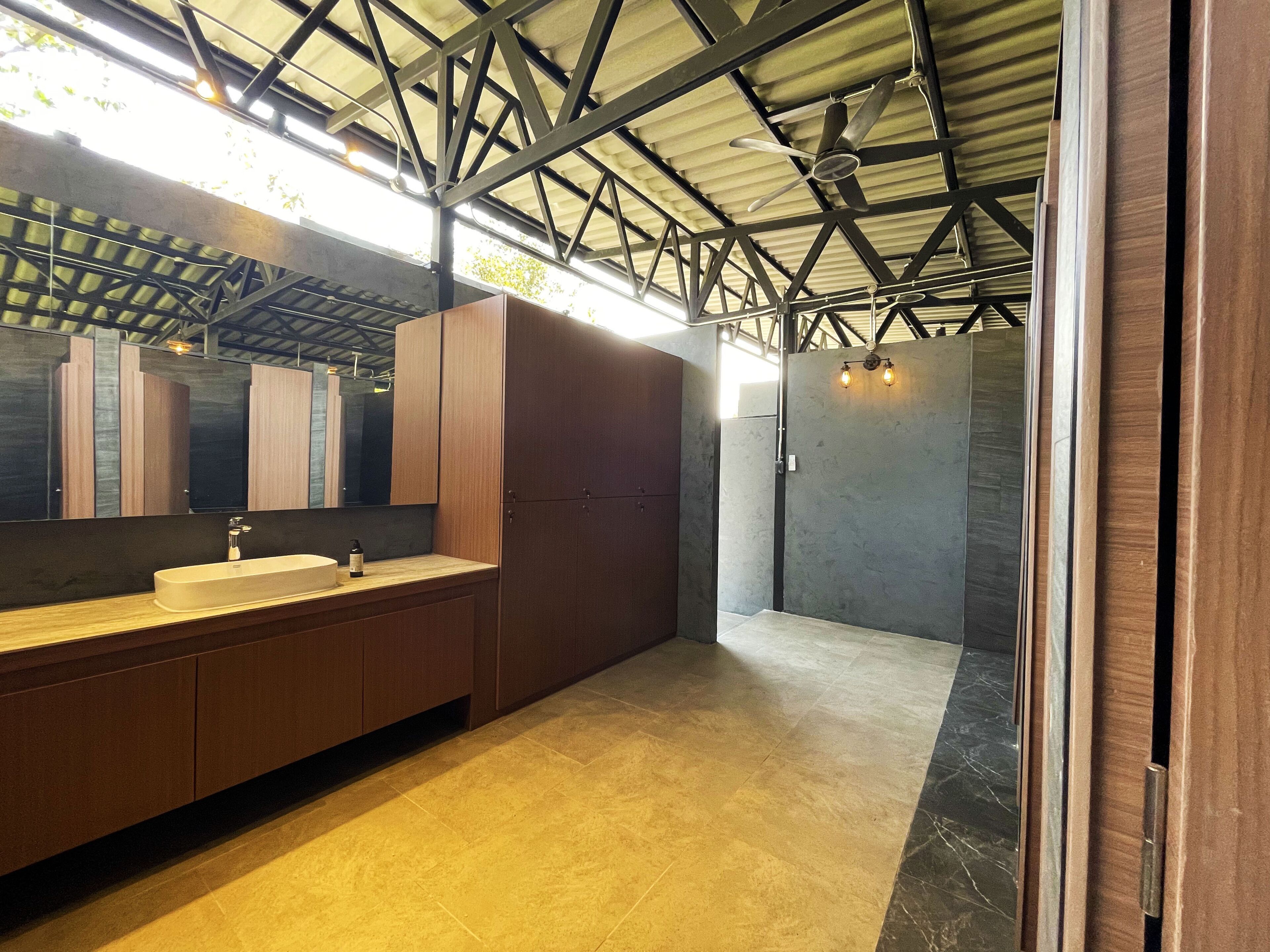 A modern bathroom with a large mirror, wooden cabinets, a sink, and a shower area.
