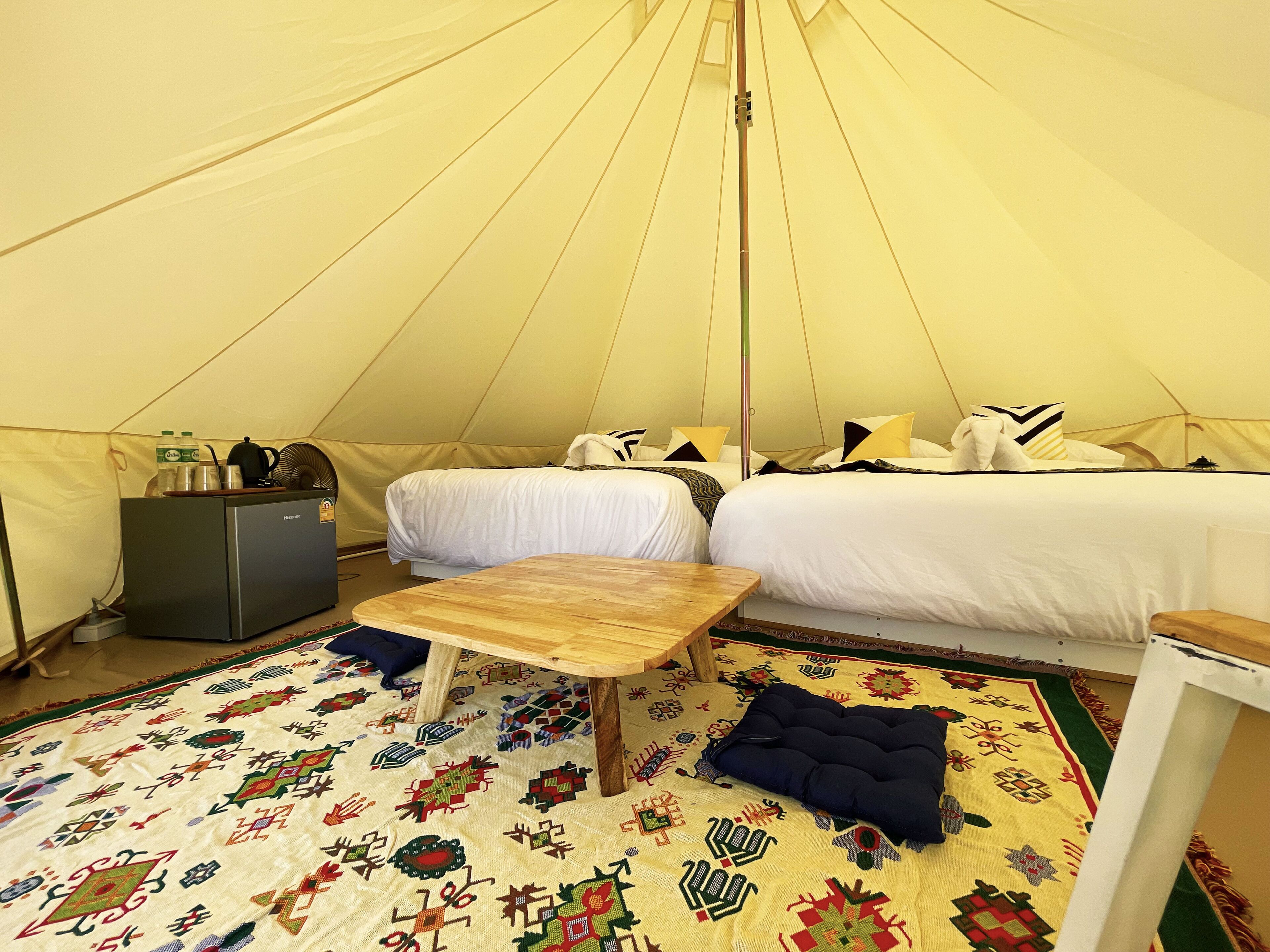 A tented accommodation with a bed, a small table, a fridge, and a patterned rug.