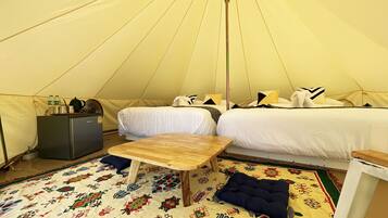 A tented accommodation with a bed, a small table, a fridge, and a patterned rug.