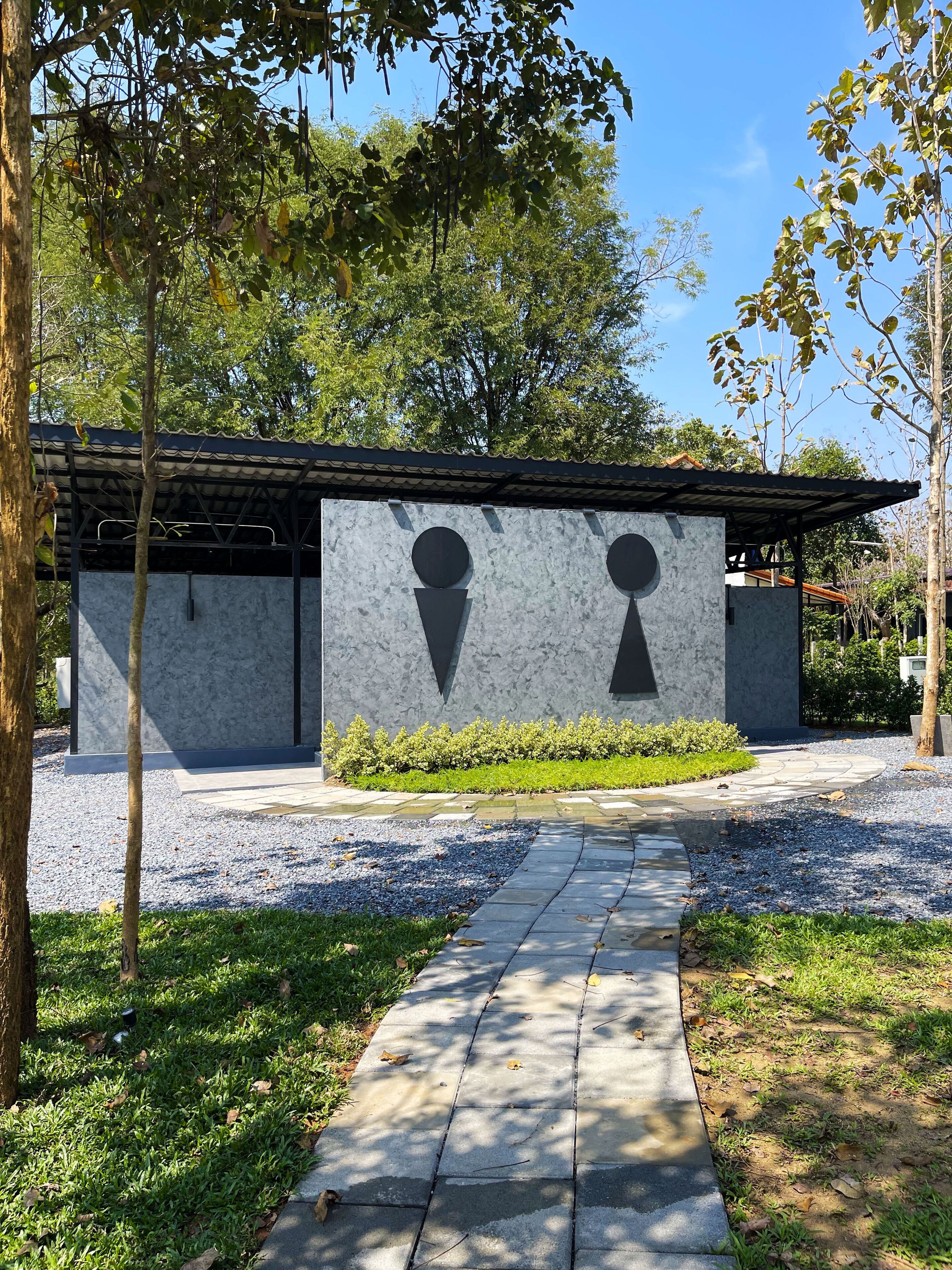 A modern building with a geometric facade, a gravel pathway, and surrounding greenery.