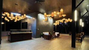 A spacious lobby with a modern design, featuring a reception desk, seating area, and hanging pendant lights.