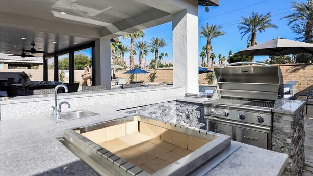 An outdoor kitchen with a built-in grill, sink, and seating area. - Moon Palace • Desert Oasis with Private Pool & Spa (Indio)