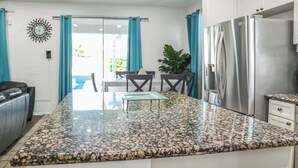 A kitchen with a granite countertop, a stainless steel refrigerator, and a dining area with a table and chairs. - Moon Palace • Desert Oasis with Private Pool & Spa (Indio)