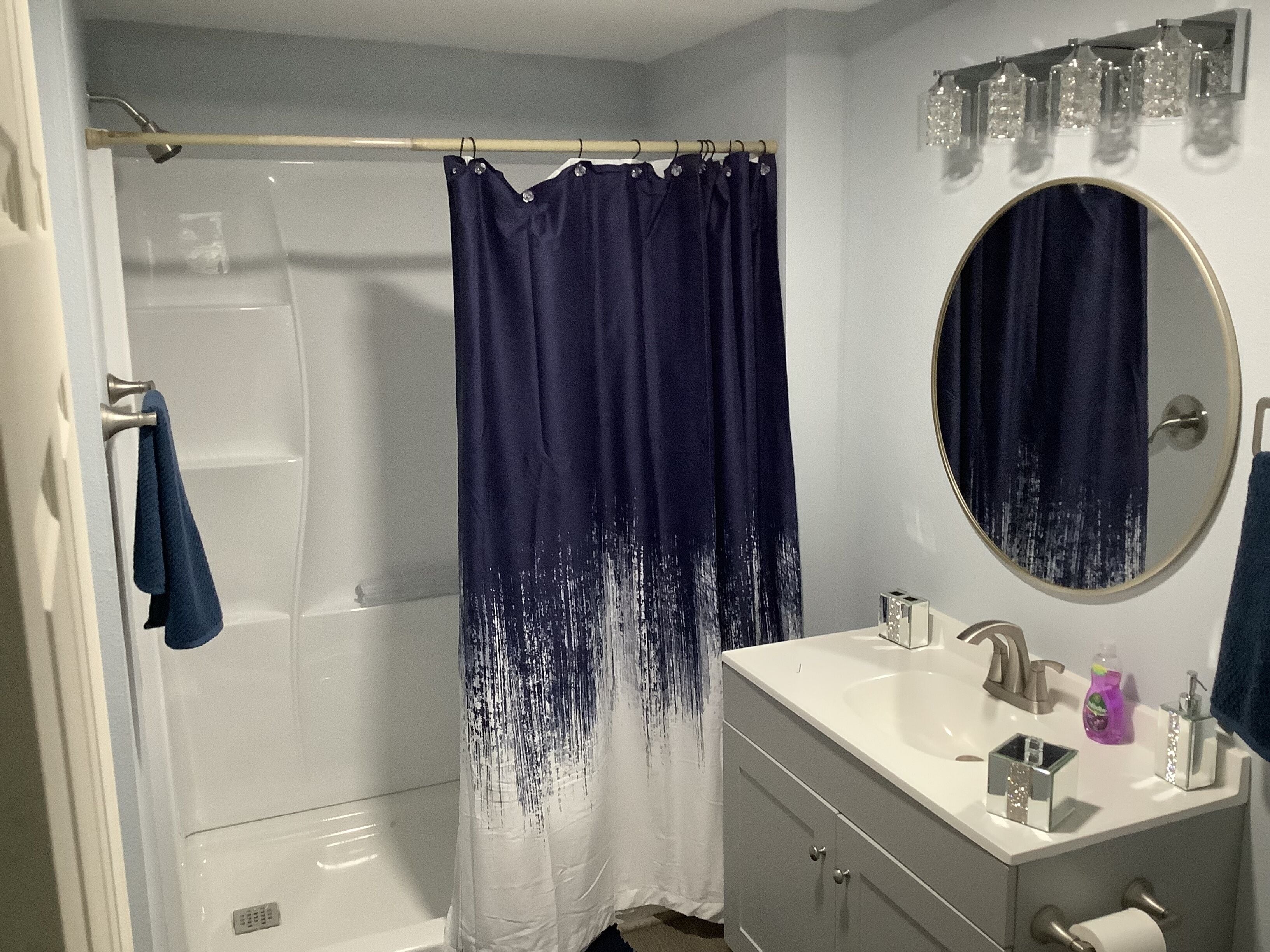 A bathroom with a shower, a sink, a mirror, and a towel hanging on the door.