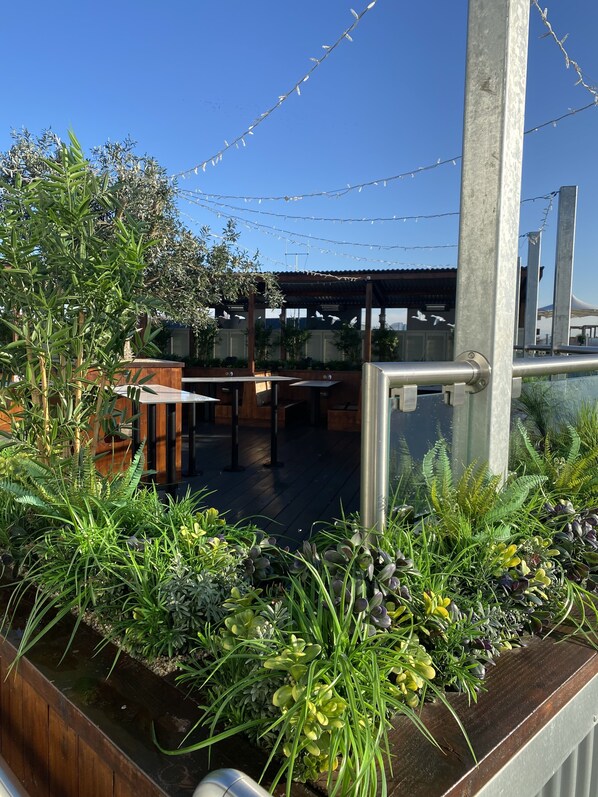 Un jardín en la azotea con diversas plantas, una mesa de madera y una barandilla de metal.