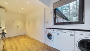 Une buanderie équipée d’un lave-linge, d’un sèche-linge et d’une fenêtre donnant sur un quartier résidentiel.