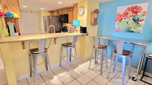 A kitchen with a bar area, a clock, and a painting on the wall. - Habitat #23 1 Bedroom Home by RedAwning (South Padre Island)