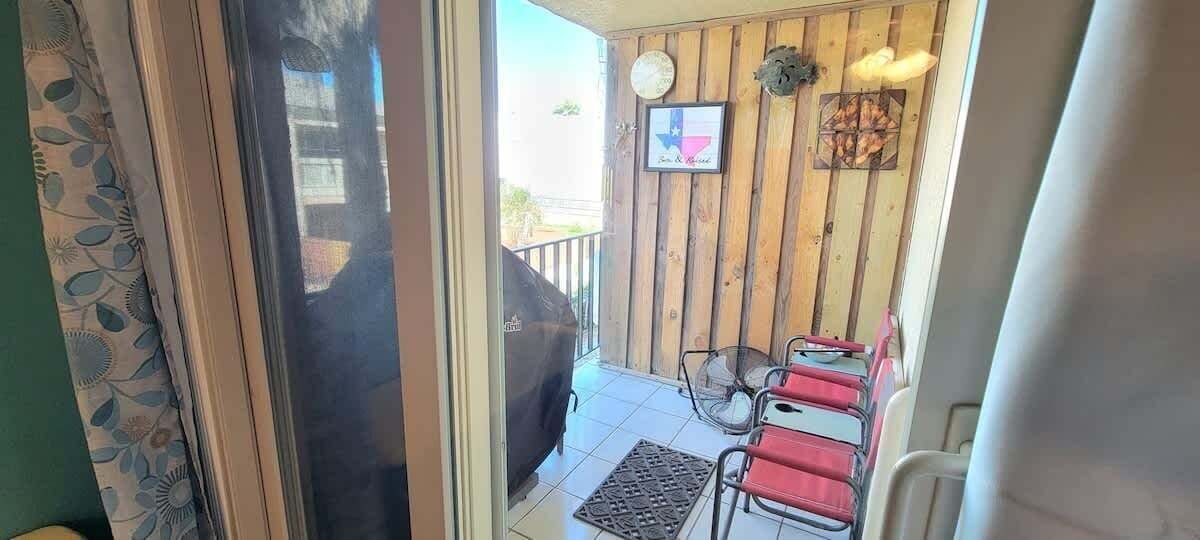 A patio area with a barbecue grill, two red chairs, and a wooden wall with a Texas flag and a clock.