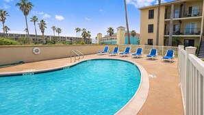 A pool with blue water, surrounded by a white fence, and blue lounge chairs. - Habitat #23 1 Bedroom Home by RedAwning (South Padre Island)