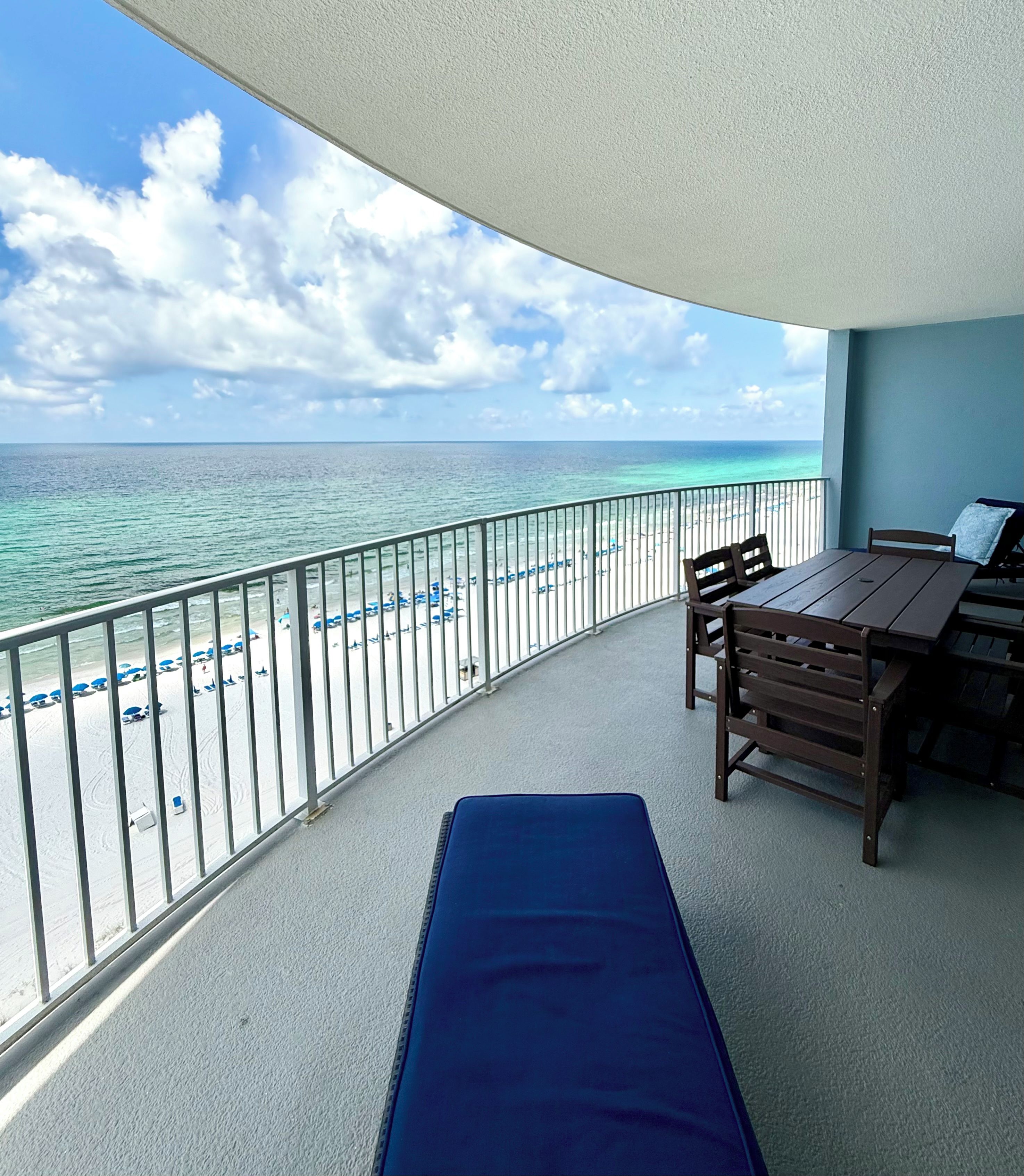 Un balcon avec vue sur l’océan, une table, des chaises et un tapis bleu.