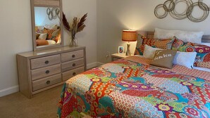 A bedroom with a large bed, a dresser, a mirror, a lamp, and decorative pillows.