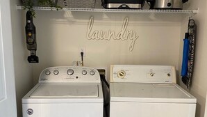 A laundry room with two white Whirlpool washers and dryers, a shelf with kitchen items, and a 'laundry' sign.