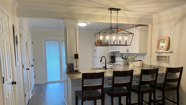 A kitchen with a central island, four barstools, a hanging light fixture, and a refrigerator.