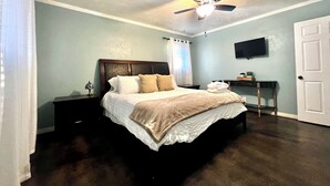 Une chambre à coucher avec un lit, une table de chevet, un ventilateur de plafond, une télévision et une porte.