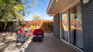 Une terrasse avec un canapé rouge et une petite table, un mur en briques et une porte vitrée donnant sur un espace abrité.