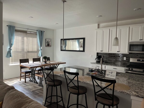 A modern kitchen with a dining area, featuring a granite countertop, stainless steel appliances, and a dining table with chairs.