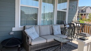 A covered porch with a gray sofa, striped pillows, a small table, and a fire pit.
