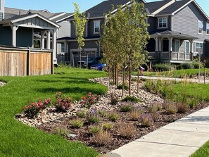 A residential area with houses, a well-maintained lawn, and a landscaped garden with various plants and flowers.