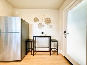Compact kitchen area with a refrigerator, dining table, and stools.