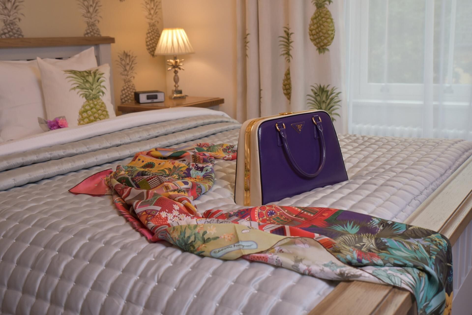 A bed with a patterned bedspread, a colorful throw blanket, and a purple handbag on the side.
