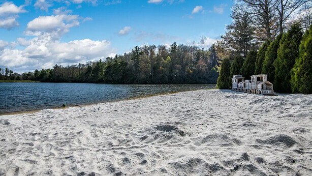 Ein Sandstrand mit einem See, Bäumen und einem kleinen Steg mit einem Boot.