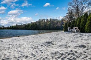 Ein Sandstrand mit einem See, Bäumen und einem kleinen Steg mit einem Boot.
