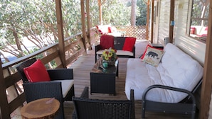 Eine Terrassenausstattung mit Korbmöbeln, ein weißes Sofa mit einem Bärenkissen und ein Tisch mit einem Blumenstrauß.
