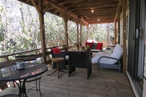 Eine überdachte Terrasse mit einem runden Tisch, zwei Stühlen, einer Couch mit Kissen und einem kleinen Tisch mit einer Vase.