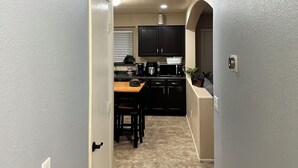 A narrow hallway leading to a kitchen with a dining area, a ceiling vent, and a door with a light switch. - Cozi 3 bedroom with pool table and full bar (Maricopa)