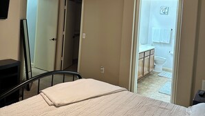 A bedroom with a bed, a ceiling fan, a TV, and a bathroom visible through an open door. - Cozi 3 bedroom with pool table and full bar (Maricopa)