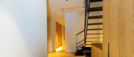 Un interior moderno con un banco de madera, una escalera y un pasillo que lleva a otra habitación.